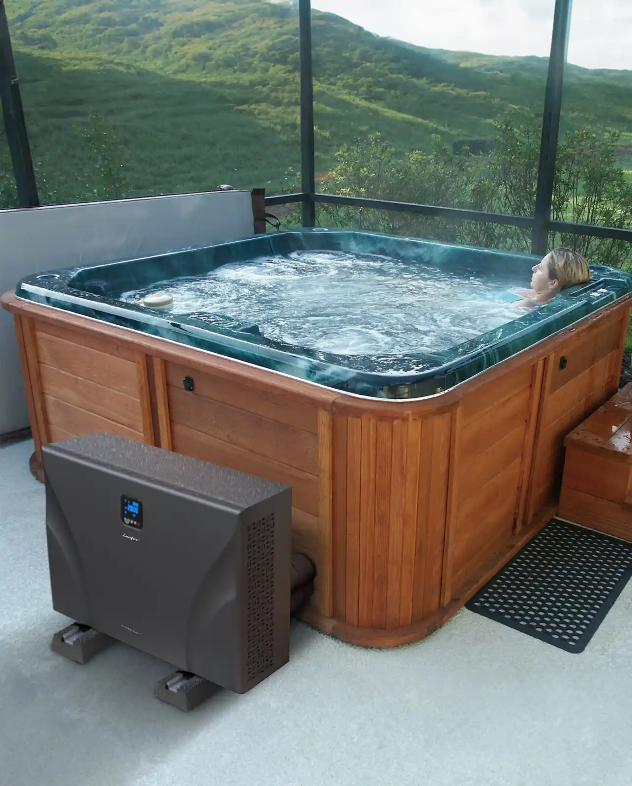 Jacuzzi din lemn cu apă în mișcare, situat într-un mediu natural, cu un utilizator relaxându-se în interior; lângă jacuzzi se află o pompă de căldură ZEALUX, de culoare închisă, cu un panou de control vizibil.