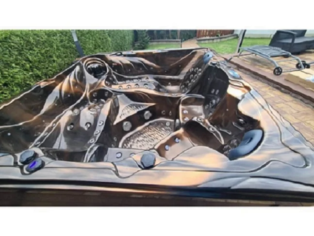 Cadă cu hidromasaj New Maximus, cu un design modern și finisaj din acril, are un interior cu forme curbe și 136 de jeturi de masaj, fiind amplasată într-un mediu exterior verde, pe o terasă din piatră.