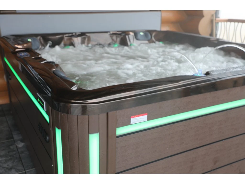 Cadă cu hidromasaj New Maximus, cu un design modern, are un finisaj din acril de culoare închisă, cu iluminare verde pe margini și apă în mișcare, situată într-un spațiu interior elegant.