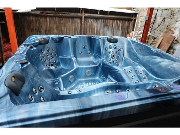 Cadă cu hidromasaj New Maximus, de culoare albastră, cu un design modern și 136 de jeturi de masaj, situată într-un mediu rustic, cu pereți din lemn și materiale de construcție expuse.