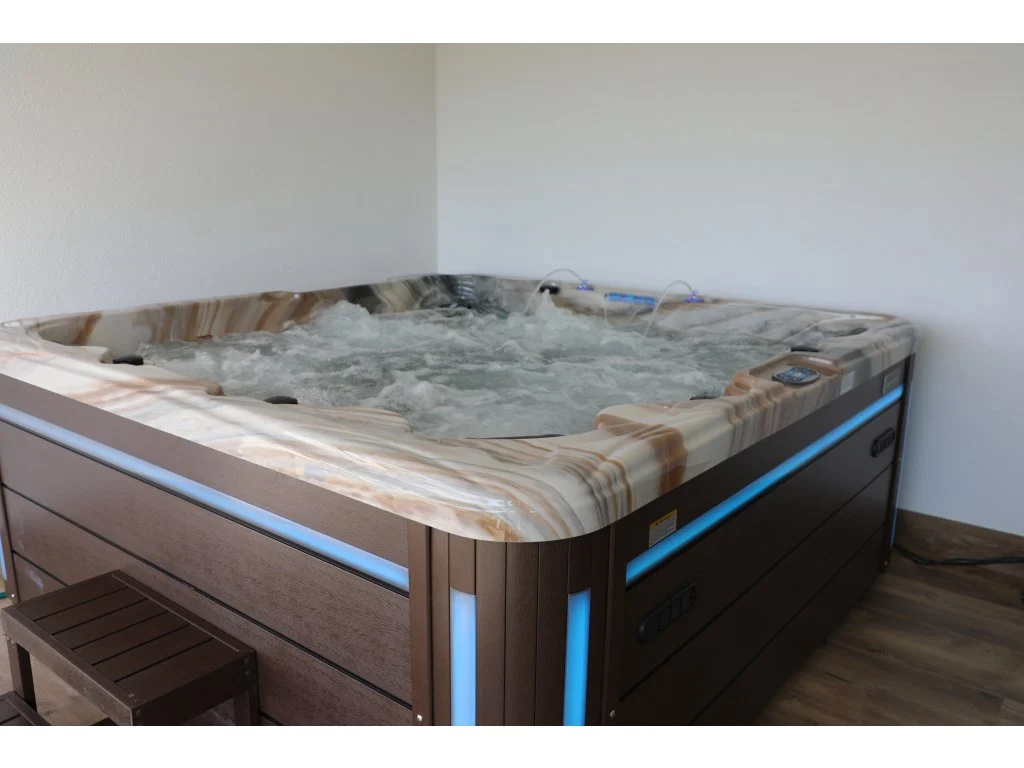 Cadă cu hidromasaj New Maximus, cu un design modern, situată într-un spațiu interior, având un finisaj din acril cu nuanțe de bej și un cadru din lemn, dotată cu lumini LED albastre și un sistem de jeturi de masaj, oferind locuri pentru 4-5 persoane.