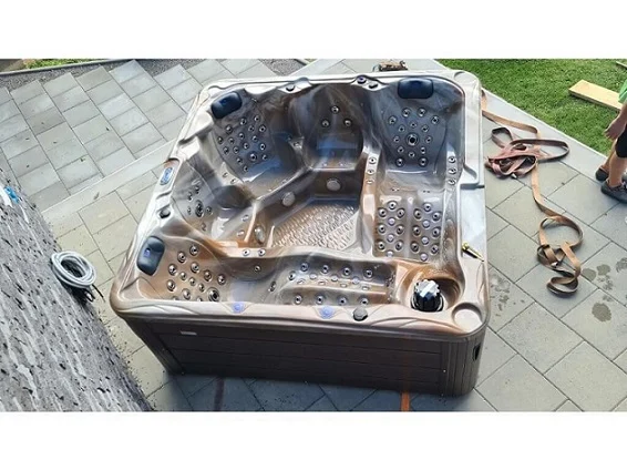 Cadă cu hidromasaj New Maximus, de formă pătrată, cu un finisaj de culoare maro, amplasată pe o suprafață de piatră, având capacitate pentru 4-5 persoane și 136 de jeturi de masaj.