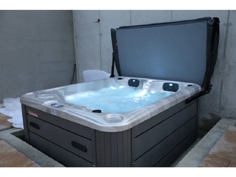 Cadă cu hidromasaj PUMA 210×170×90 cm, cu un design compact și confortabil, situată într-un mediu interior, cu un capac deschis, având un interior cu apă și lumini integrate, realizată din acril, cu carcasă de culoare gri.