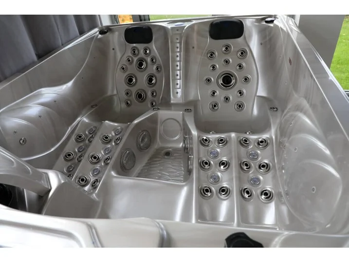 Cadă cu hidromasaj PUMA 210×170×90 cm, cu un interior argintiu lucios, dotată cu numeroase jeturi de masaj, două șezlonguri ergonomice și un loc de ședere, amplasată într-un mediu interior cu feronerie neagră.