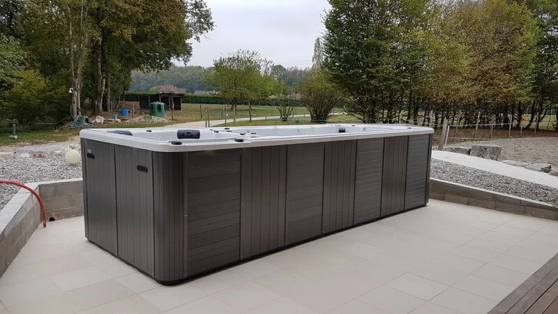 Spa & Swim Spa 801 este un spa de dimensiuni mari, cu un design modern, realizat dintr-un material de culoare gri, situat pe o terasă din piatră, înconjurat de un peisaj natural cu copaci și iarbă verde.