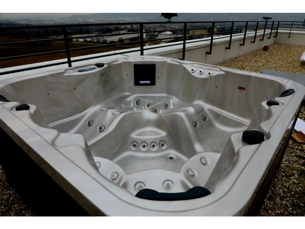 Cadă cu hidromasaj SPLIT 200×200×90 cm, cu un design modern și ergonomic, situată pe o terasă, având un interior din acril de culoare deschisă, cu multiple jeturi de masaj, potrivită pentru 4-5 persoane.