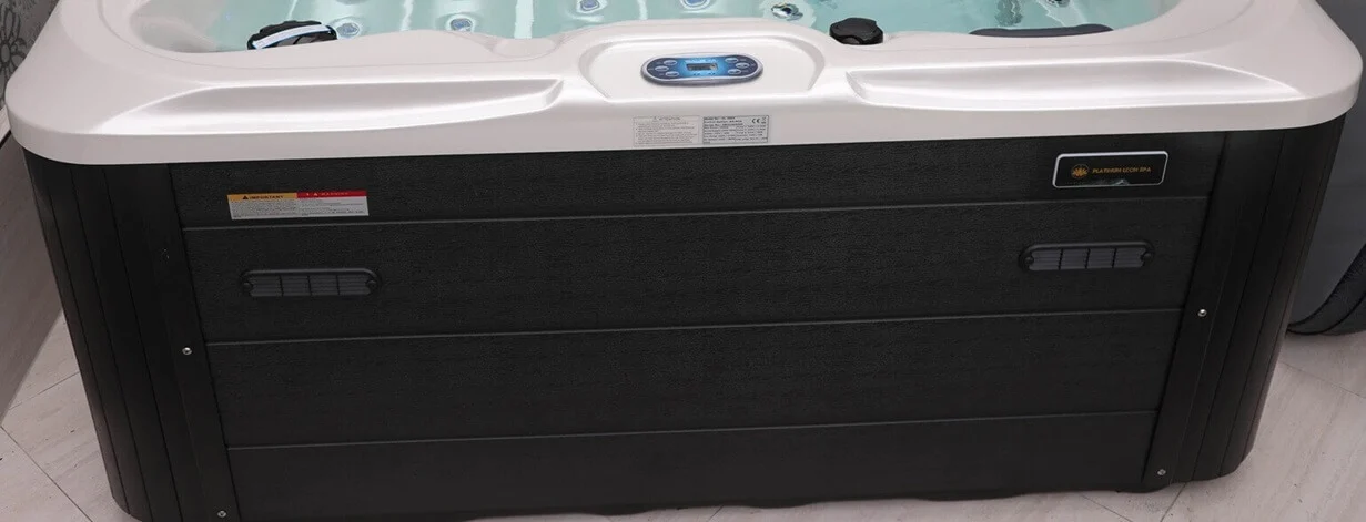 Cadă cu hidromasaj New Maximus LIFE, cu un design modern, având un exterior din material negru și un capac alb, situată pe o suprafață de podea deschisă, cu un panou de control digital vizibil.