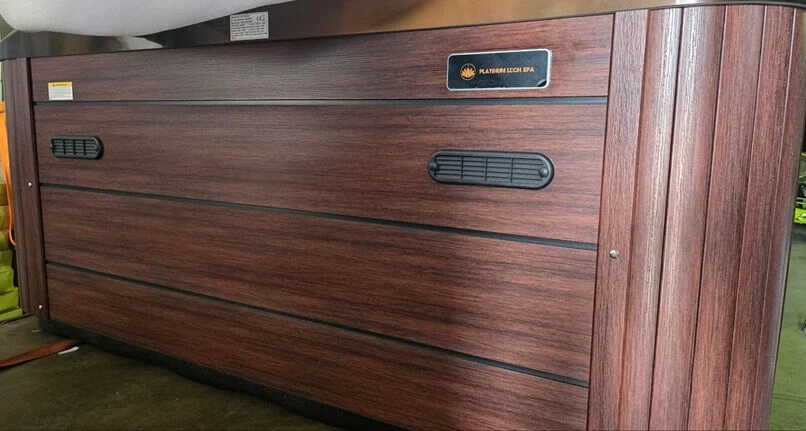 Cadă cu hidromasaj New Maximus LIFE, cu un finisaj din lemn de culoare maro, având un design elegant și linii curate, cu grile de ventilație negre și un logo metalic pe panoul frontal.
